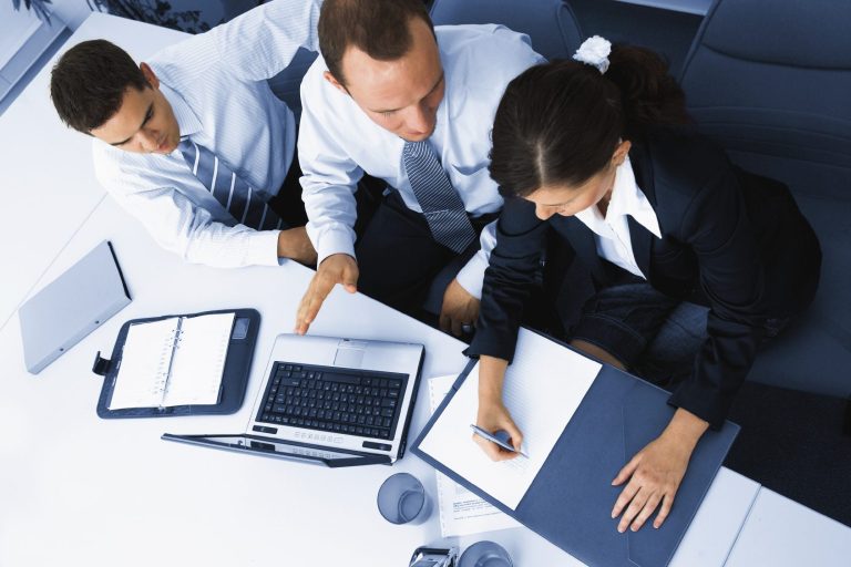Three professionals collaborate at a table with laptops and documents.