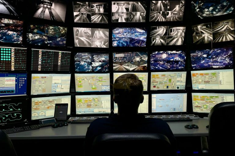A person monitoring multiple screens displaying surveillance footage and data.