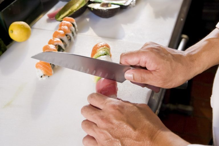 A chef's hands slicing sushi rolls on a white cutting board.