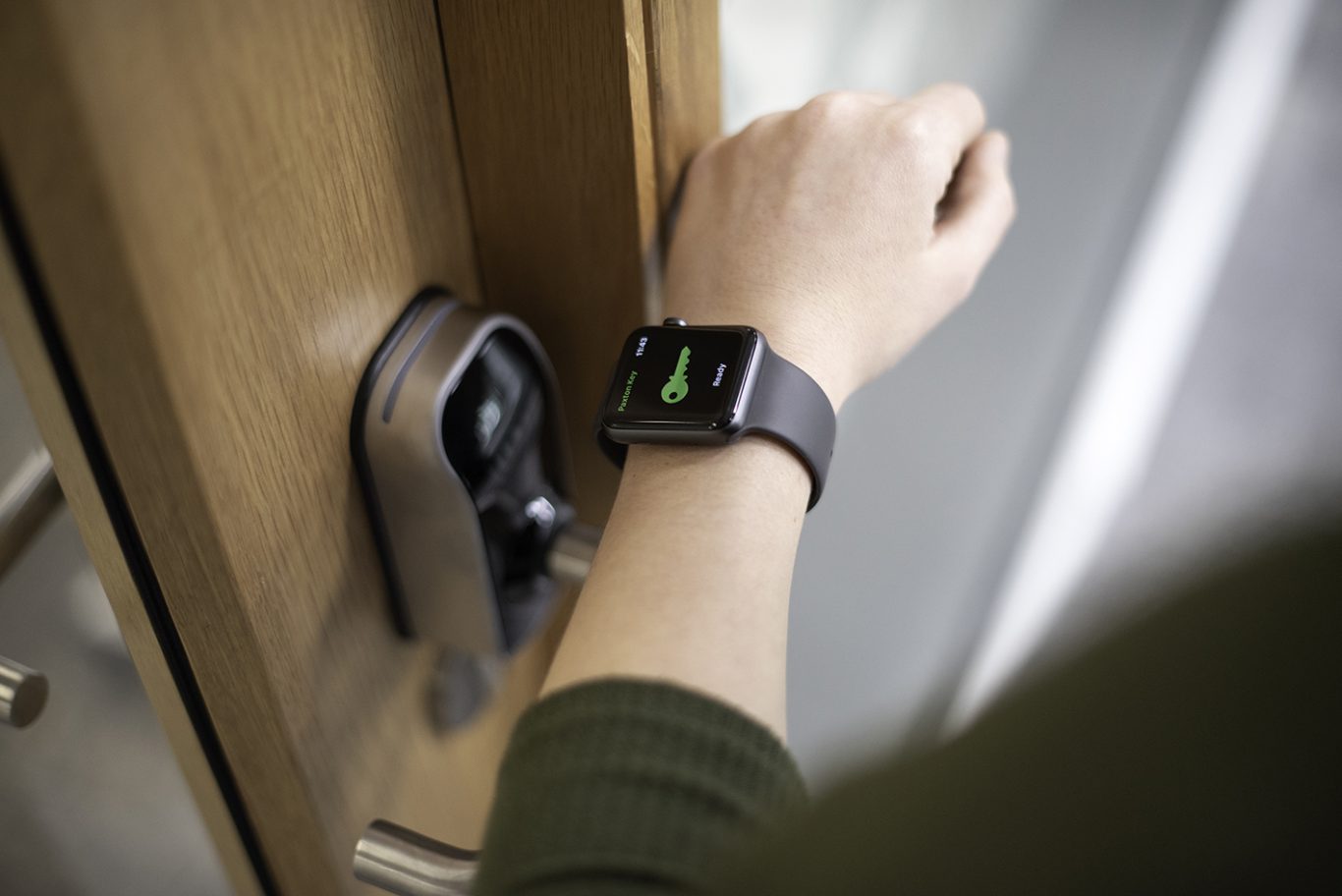 A hand with a smartwatch unlocks a door with a smart lock.
