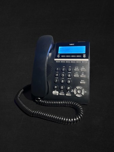 Corded telephone with a digital display and keypad, set against a dark background.